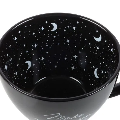A black ceramic cup with white crescent moons and stars on a glossy night-sky interior.