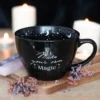 A black ceramic mug with “Make your own Magic” text surrounded by candles and dried flowers.