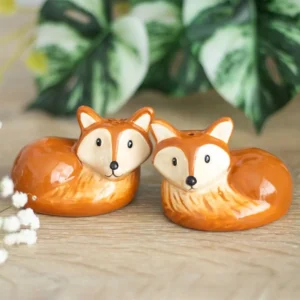 Fox Salt and Pepper Shakers Ceramic Orange - Cozy Home Decor Two orange ceramic fox salt and pepper shakers on a light wooden surface with greenery.