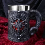 A gothic mug with a goat head, pentagram, and horn handle on red velvet fabric.