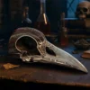 Raven Skull Sculpture Metallic Silver - Gothic Etched Design Metal raven skull sculpture on a wooden table in a dimly lit gothic study.