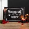 Gothic Wooden Black Sign Decor - Red Roses And Melted Candles Black gothic “Welcome to Our Crypt” sign with red roses and melting black candles on a table.