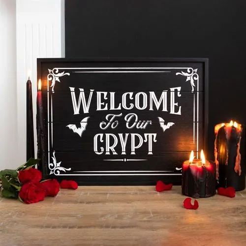 Gothic Wooden Black Sign Decor - Red Roses And Melted Candles Black gothic “Welcome to Our Crypt” sign with red roses and melting black candles on a table.