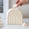 Ceramic Arch Wax Melt Warmer - Matte Cream Minimalist Design A hand placing a wax cube into a cream ceramic arch warmer on a white tabletop.