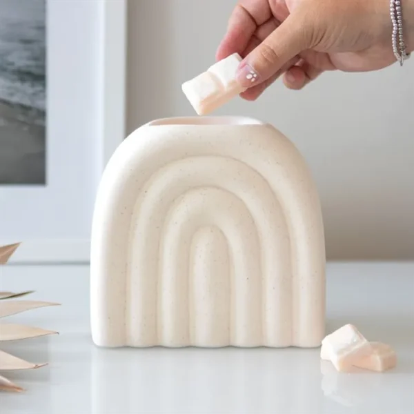Ceramic Arch Wax Melt Warmer - Matte Cream Minimalist Design A hand placing a wax cube into a cream ceramic arch warmer on a white tabletop.