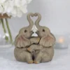 Baby Elephant Figurine Stone Texture Gray - Heart Trunk Embrace Two baby elephant figurines touching trunks to form a heart beside a candle and white flowers.