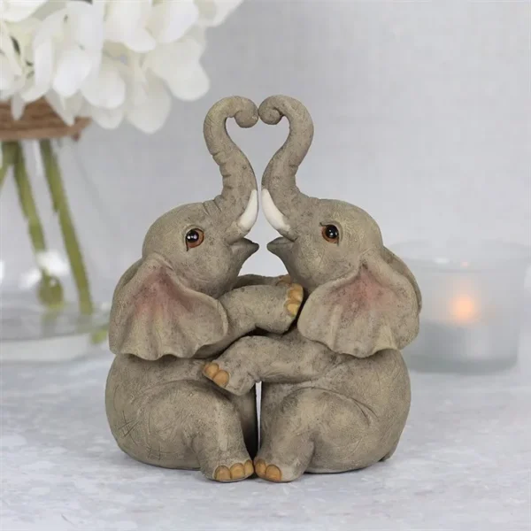 Baby Elephant Figurine Stone Texture Gray - Heart Trunk Embrace Two baby elephant figurines touching trunks to form a heart beside a candle and white flowers.