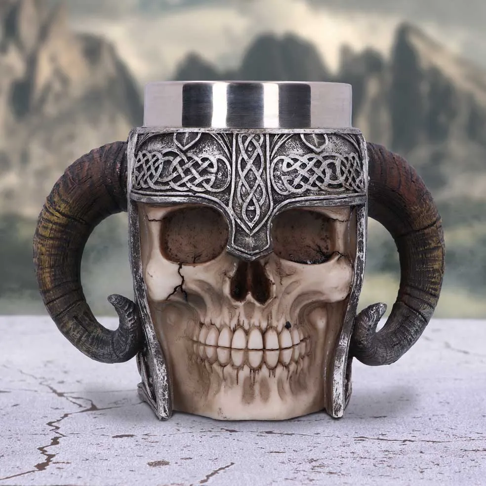 A Viking skull mug with ram horns and metallic helmet on a stone surface.