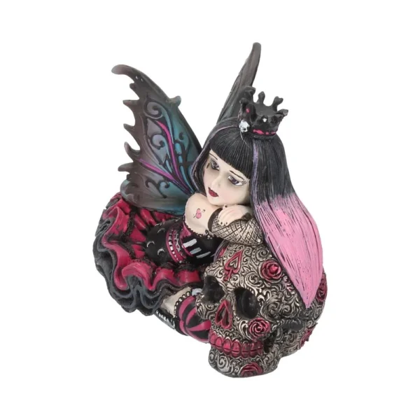 Gothic fairy figurine with turquoise wings sitting beside an ornate skull decorated with red roses.