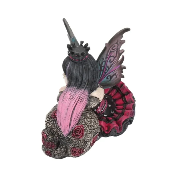 A gothic fairy figurine with black and pink hair sitting on a decorated skull with rose details.