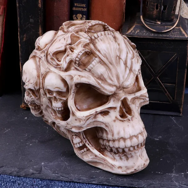 Carved Skull Ornament Resin Sculpture - Ivory With Mini Skulls An intricately carved skull ornament covered with smaller skulls on a dark textured surface.