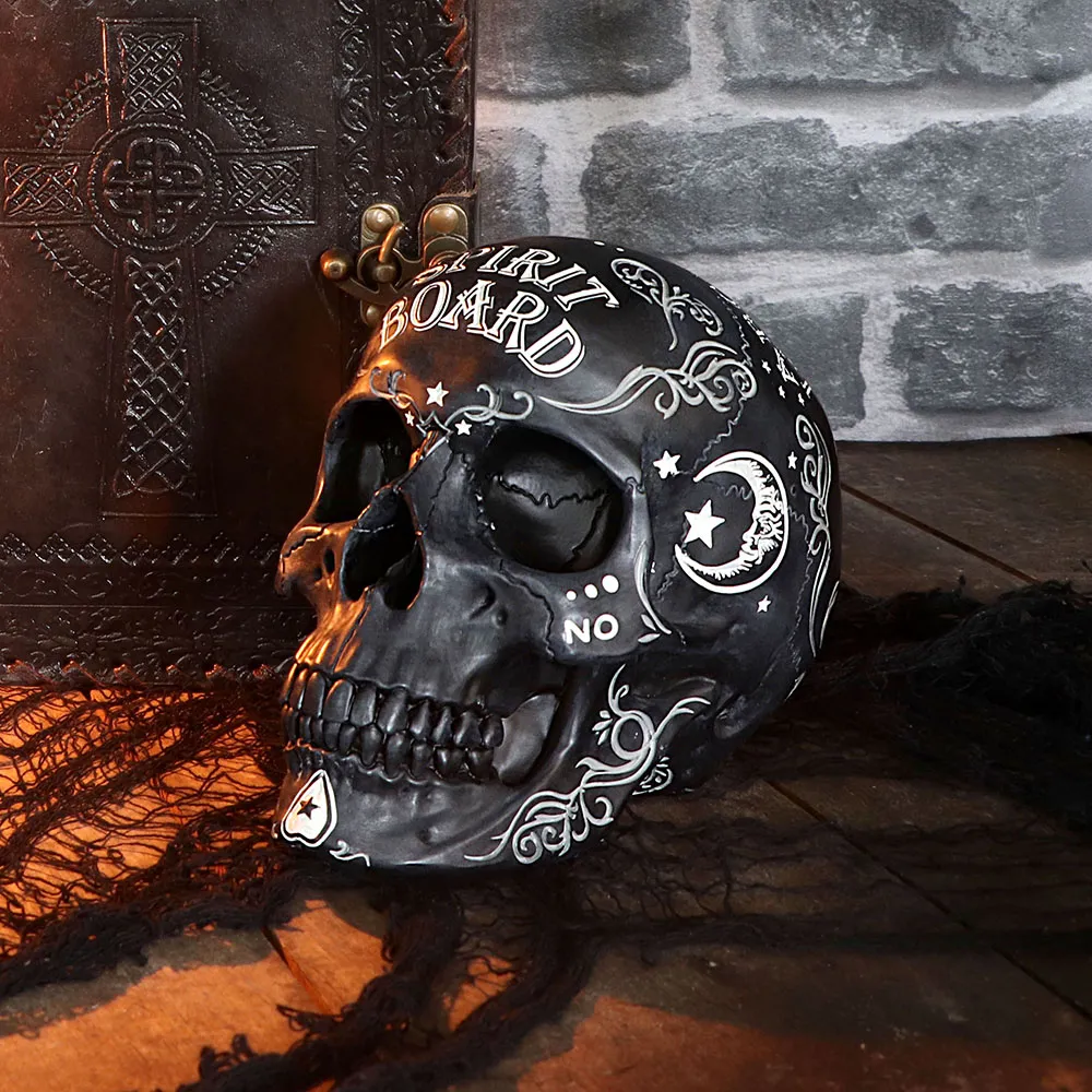 Top Halloween Party Tableware Picks 5 A black decorative spirit board skull beside an embossed leather book on a wooden surface.