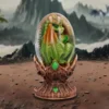 Green Dragon Egg Sculpture Glass Ornament - Bronze Stand A green baby dragon curled inside a transparent egg on an ornate golden stand in rocky mountains.