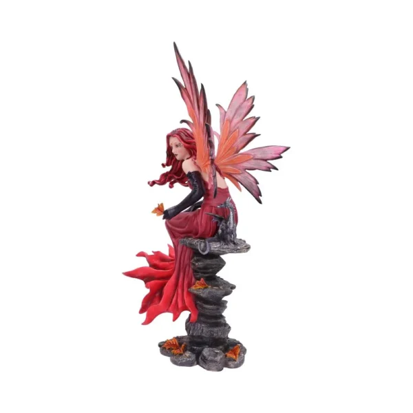 A red-dressed fairy figurine with butterfly wings sitting on dark rocks holding an orange butterfly.