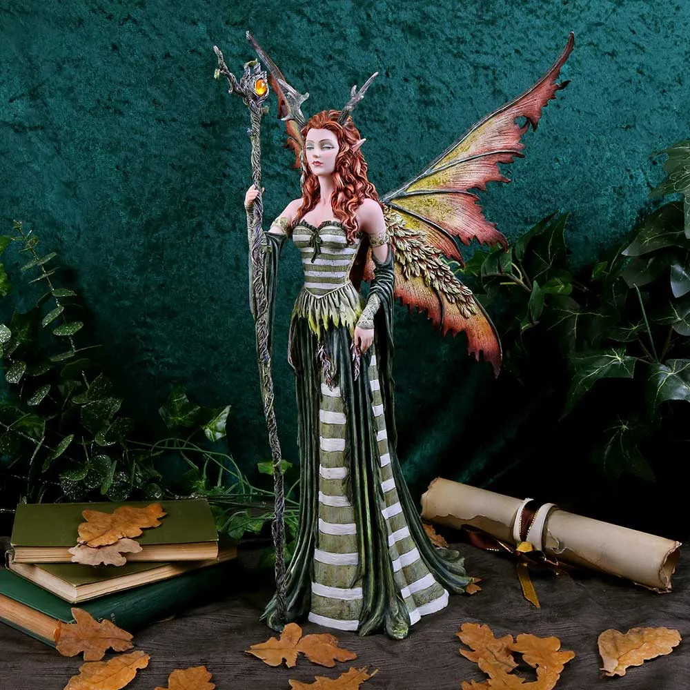 A detailed fairy figurine with autumn-colored wings holding a vine staff amid forest-themed decor.