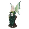 A green fairy figurine with silver hair writing on a scroll while sitting on a tree stump.