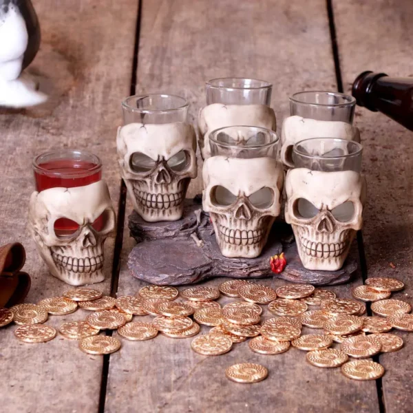 Skull Shot Glass Set Resin Base Gold Coins Rustic Tavern Style Six skull-shaped shot glasses with red liquor and gold coins on a rustic wooden table.